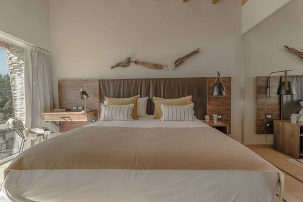A modern bedroom with a large bed, wooden headboard, bedside tables, and a view of the outdoors.