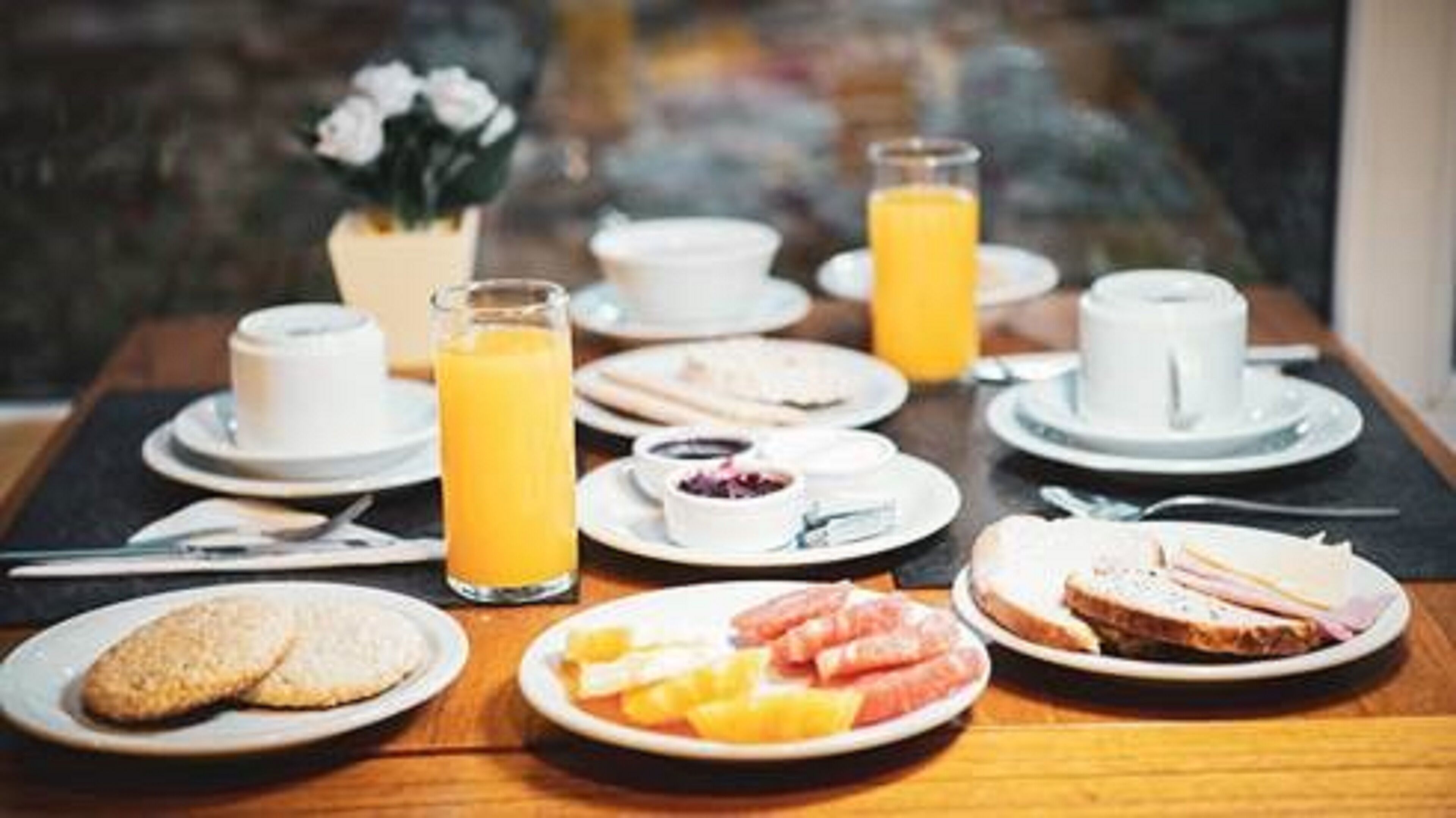 A breakfast setting with plates of food, glasses of orange juice, and cups on a table.