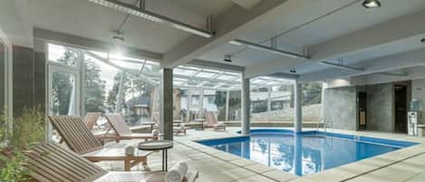 A modern indoor swimming pool area with sun loungers and a clear view of the outdoors.