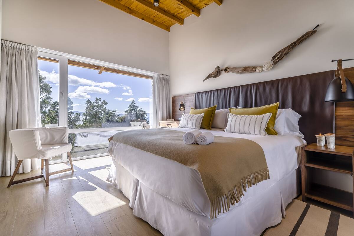 A spacious bedroom with a large bed, a wooden headboard, and a view of the outdoors.