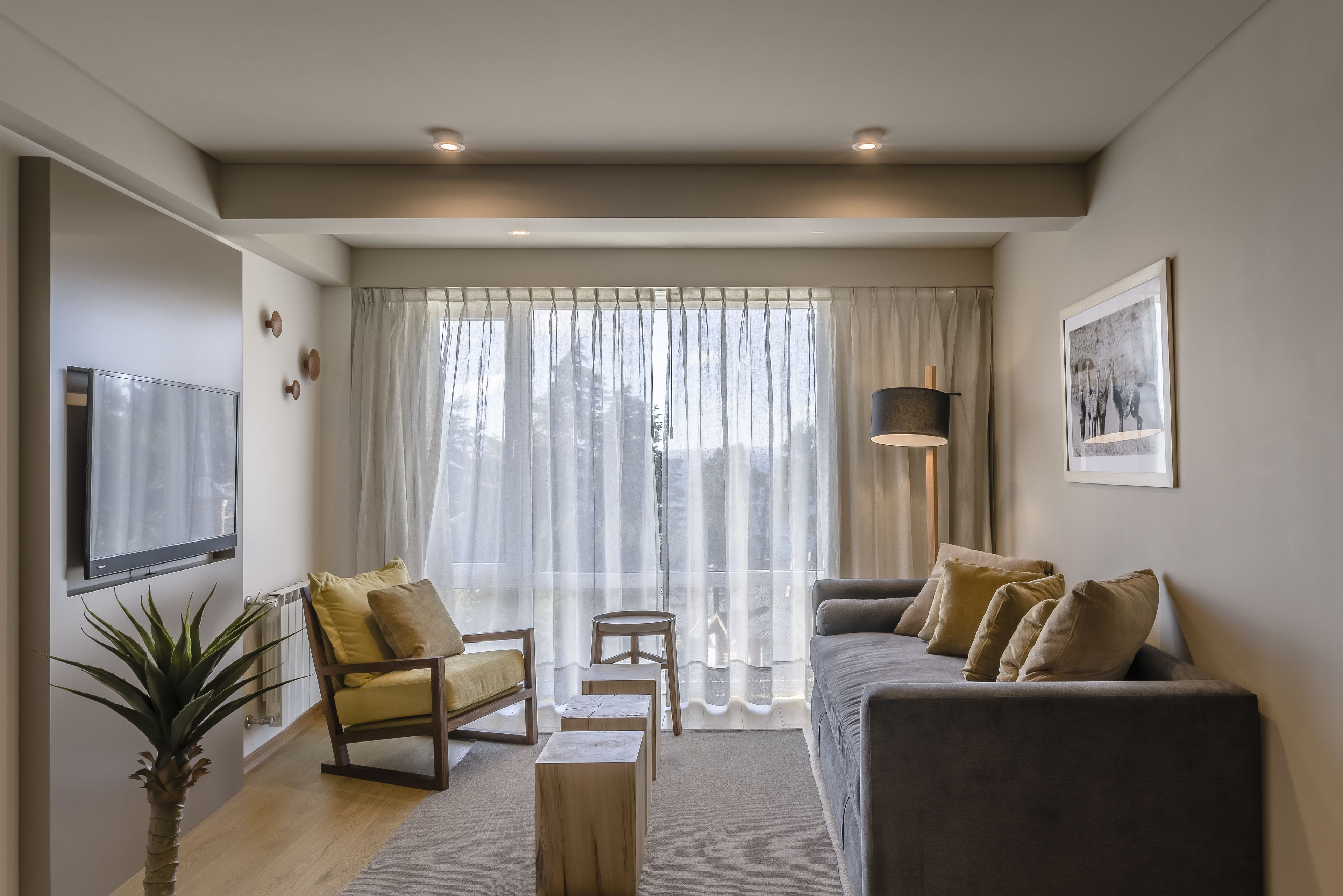 A modern living room with a sofa, armchair, and a TV mounted on the wall.