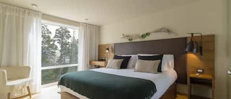 Un dormitorio moderno con una cama grande, una silla, una mesita de noche y vistas al exterior.