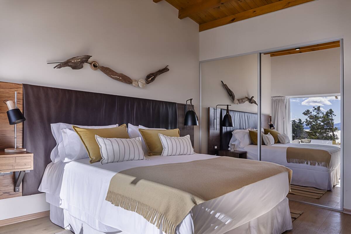 A modern bedroom with a large bed, a wooden headboard, and a mirror reflecting the room.