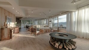 Amplia sala de estar con chimenea, muebles de madera y ventanas grandes que ofrecen vistas al exterior.