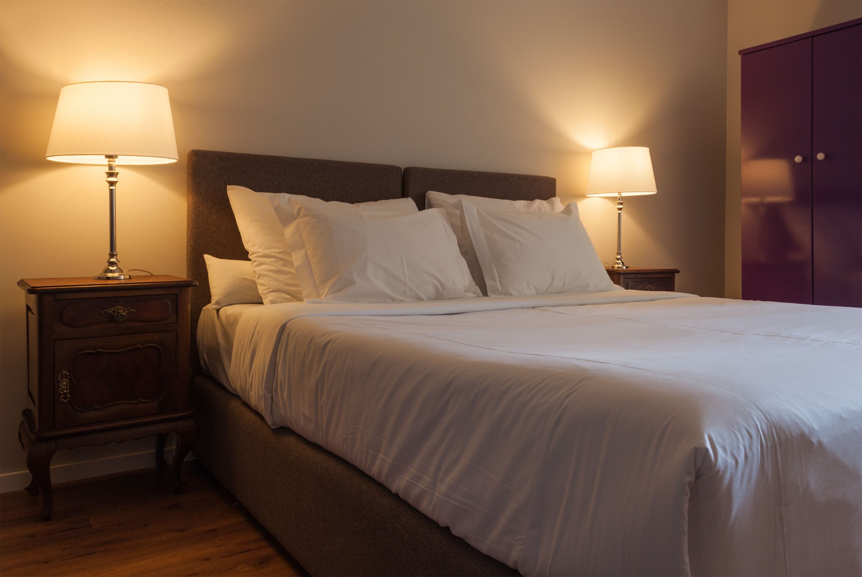 A neatly made bed with white linens and two bedside lamps on wooden nightstands.