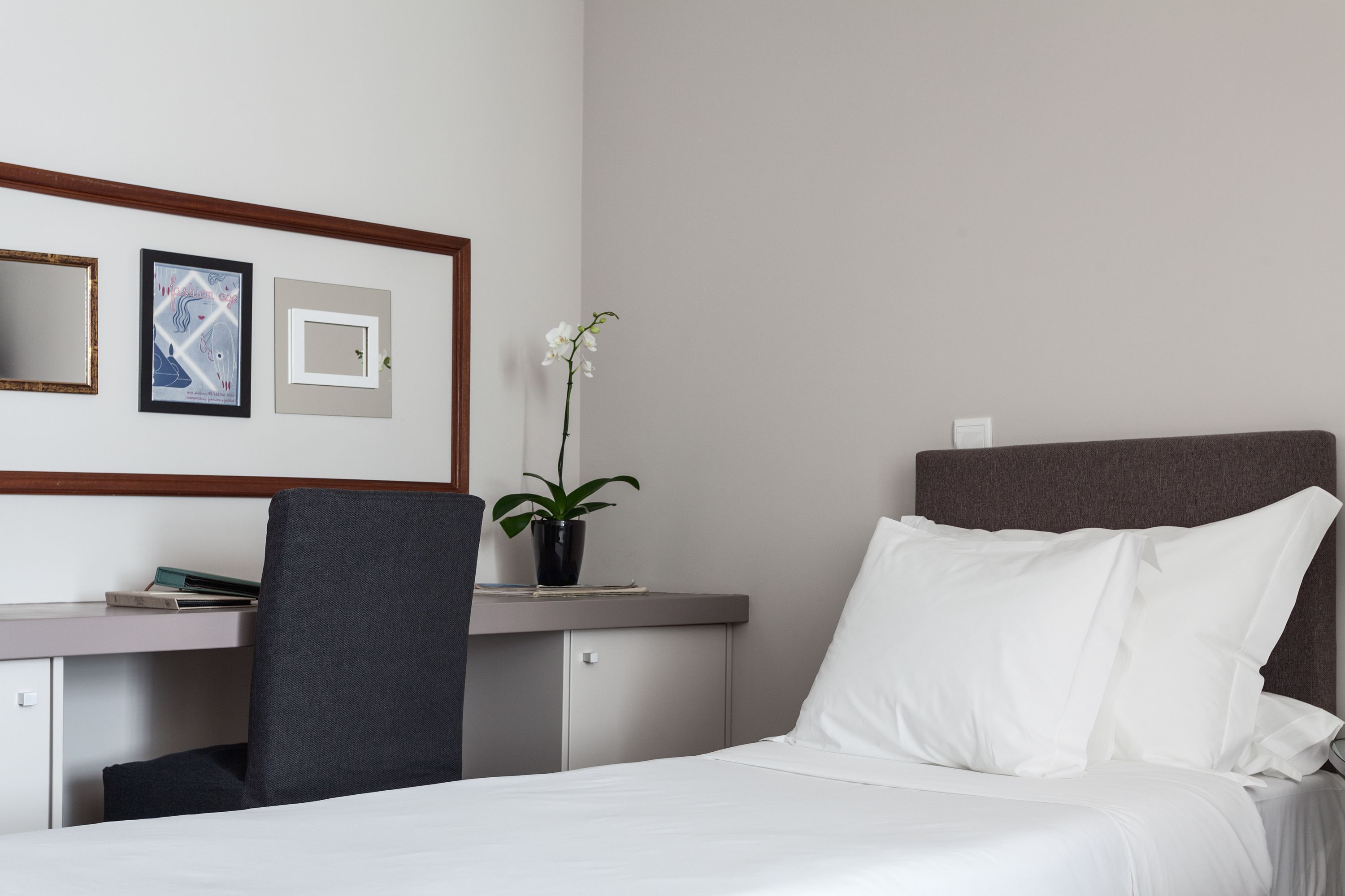 Quarto de hotel com cama, escrivaninha, cadeira, planta em vaso e quadros nas paredes.