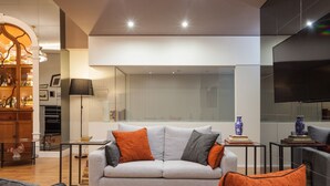 A modern living room with a grey sofa, orange and grey cushions, a flat-screen TV, and a bookshelf. - B The Guest Downtown (Porto)