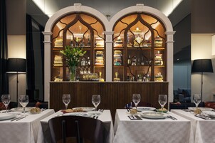 Restaurante com mesas preparadas para refeições, área de bar com estante de livros e um arco decorativo.