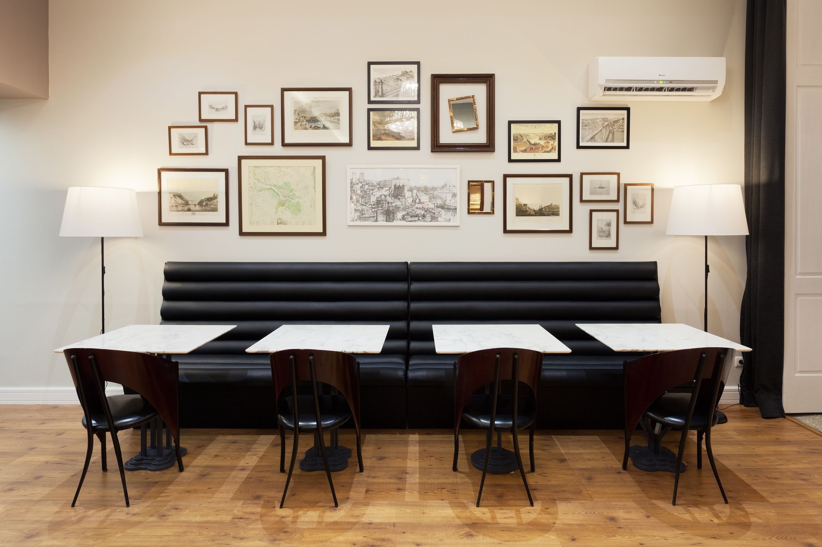 A room with a black leather sofa, three white tables, and chairs, and framed pictures on the wall.