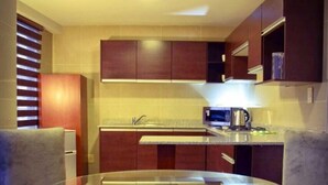 A compact kitchen with dark wooden cabinets, a glass-top dining table, and two grey upholstered chairs. - HB Sopocachi (La Paz)