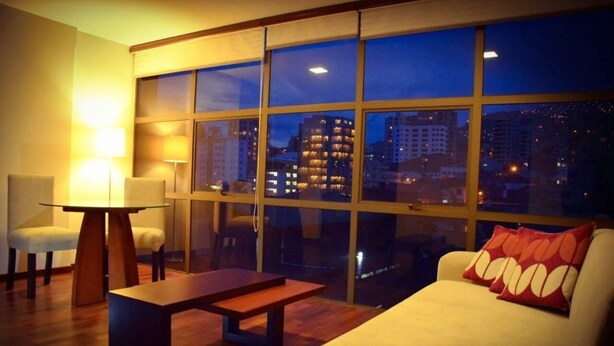 A modern hotel room with a large window, a sofa, a table, and two chairs. - HB Sopocachi (La Paz)