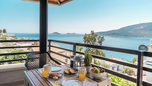 Varanda com mesa posta para o pequeno-almoço, com vista para o mar e colinas.