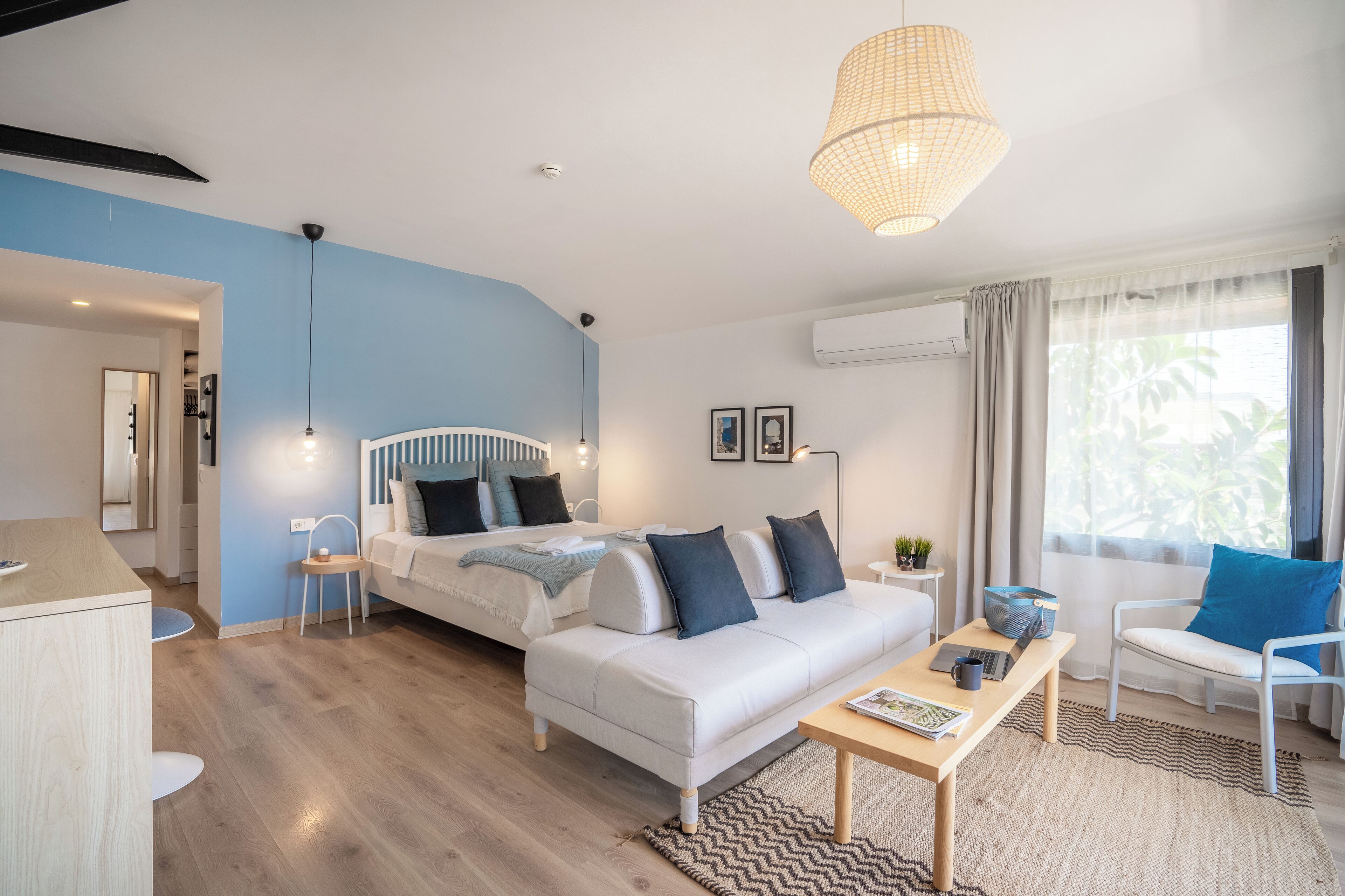 A modern bedroom with a bed, a white sofa, a wooden coffee table, and a hanging light fixture.
