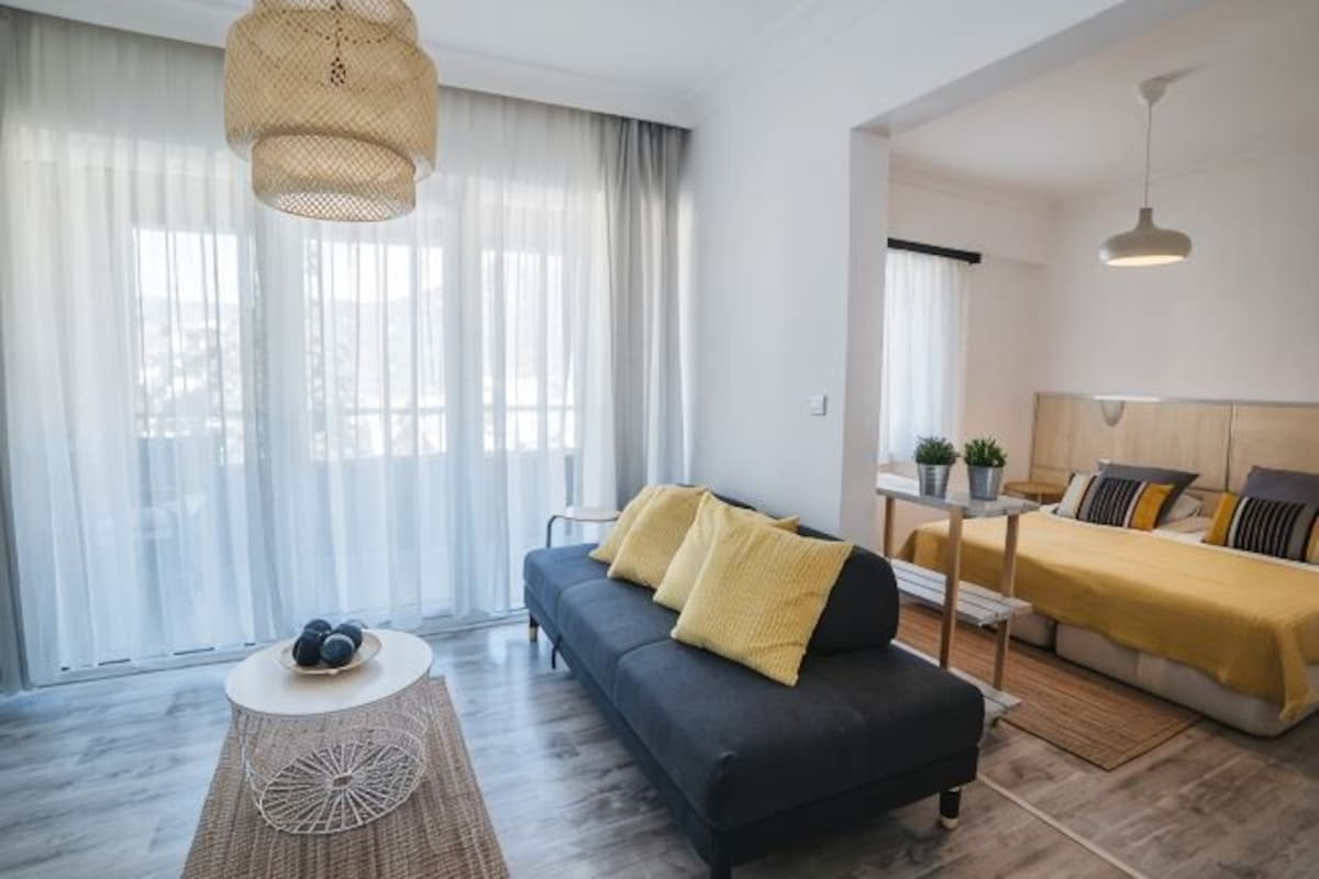 A modern living room with a sofa, a coffee table, and a bed with a yellow blanket.