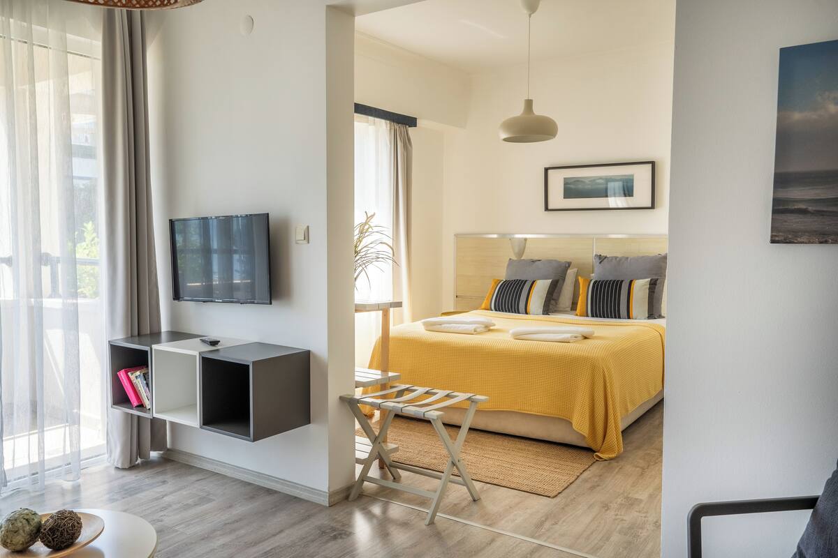 Un dormitorio moderno con cama, televisor, mesita de noche y ventana con cortinas.