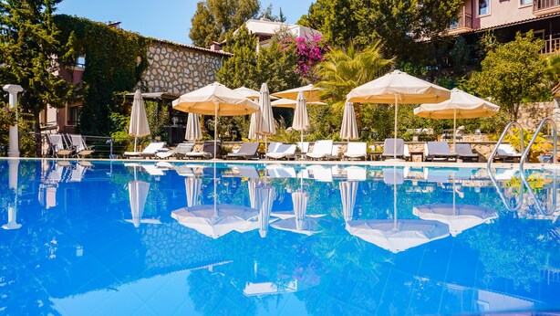 Piscina com espreguiçadeiras e guarda-sóis, cercada por vegetação e um muro de pedra.