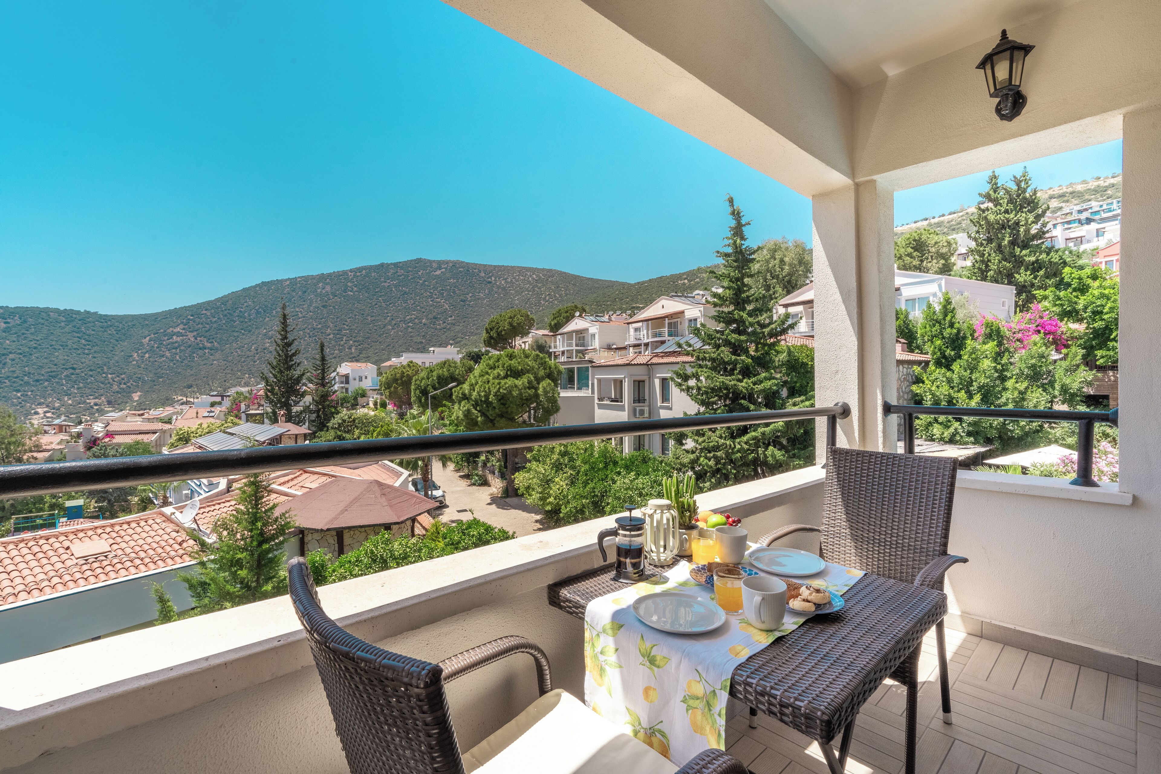 A balcony with wicker chairs, a table with breakfast items, and a view of a hillside town.