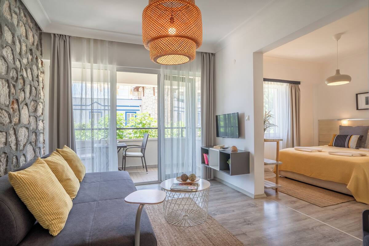 Una sala moderna con sofá, mesa de centro, televisor y cama con colcha amarilla.