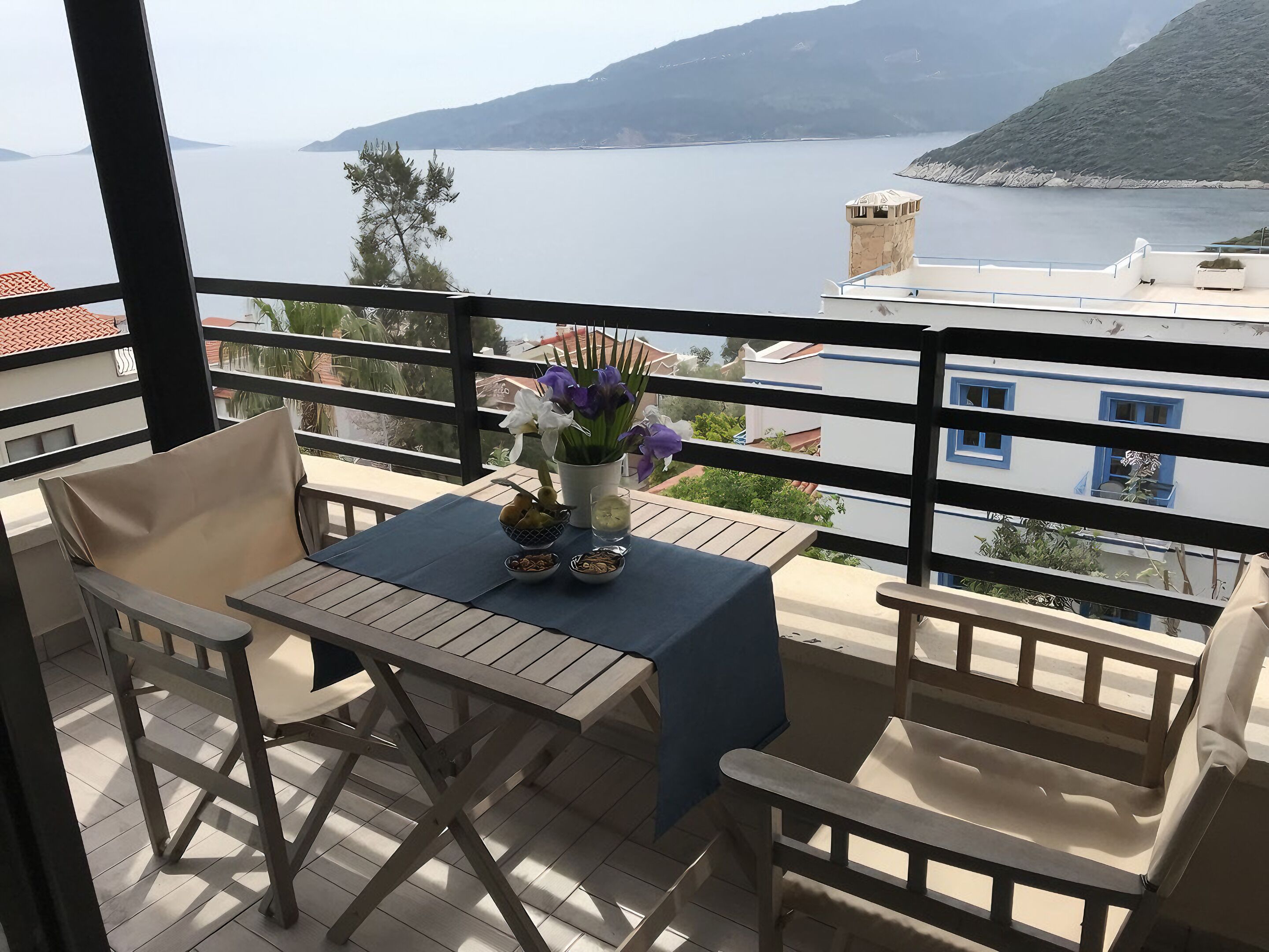 A balcony with a table, chairs, and a vase of flowers.