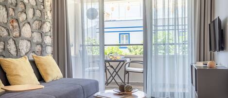 Una sala de estar moderna con un sofá gris, cojines amarillos, una mesita redonda con objetos decorativos, una pared de piedra y vistas a un balcón con mobiliario exterior.