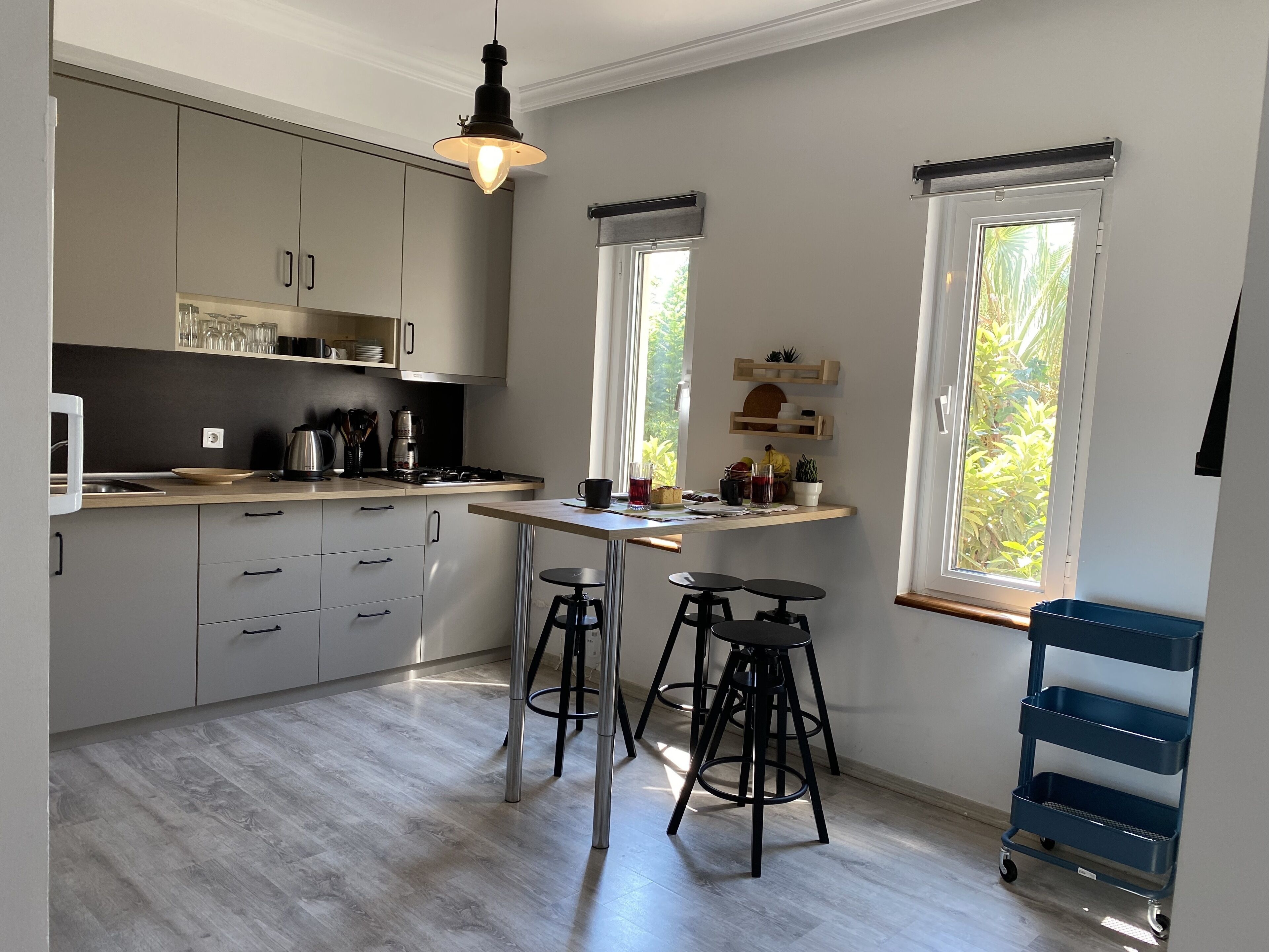 A modern kitchen with grey cabinets, a wooden countertop, a gas stove, and a hanging light fixture. There are two stools and a blue cart.