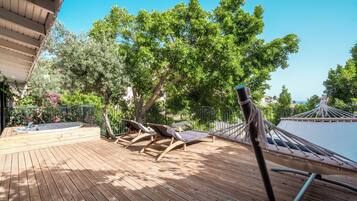 A wooden deck with lounge chairs and a hammock, surrounded by trees and a pool.
