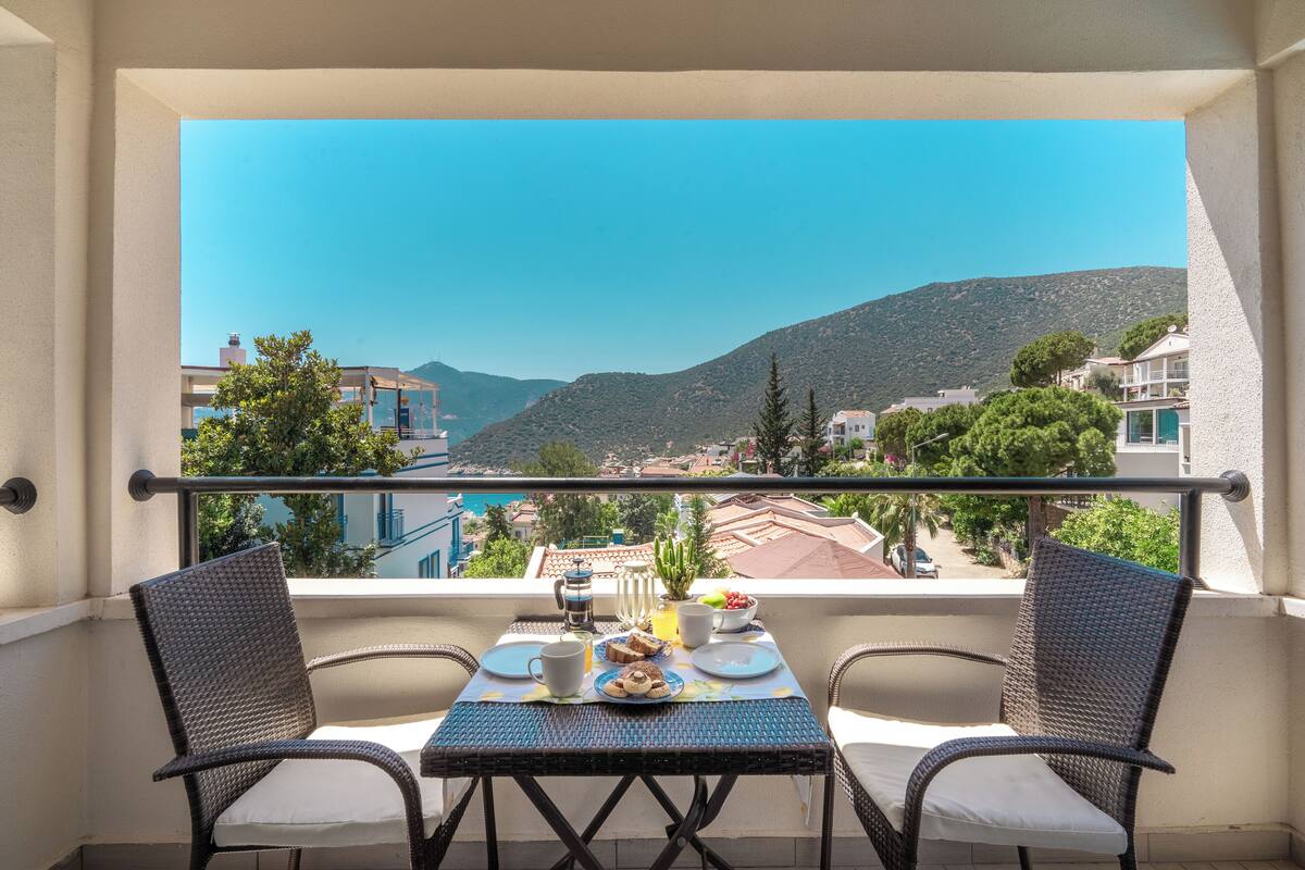 Un balcón con una mesa dispuesta para dos personas, con vistas a un paisaje montañoso.