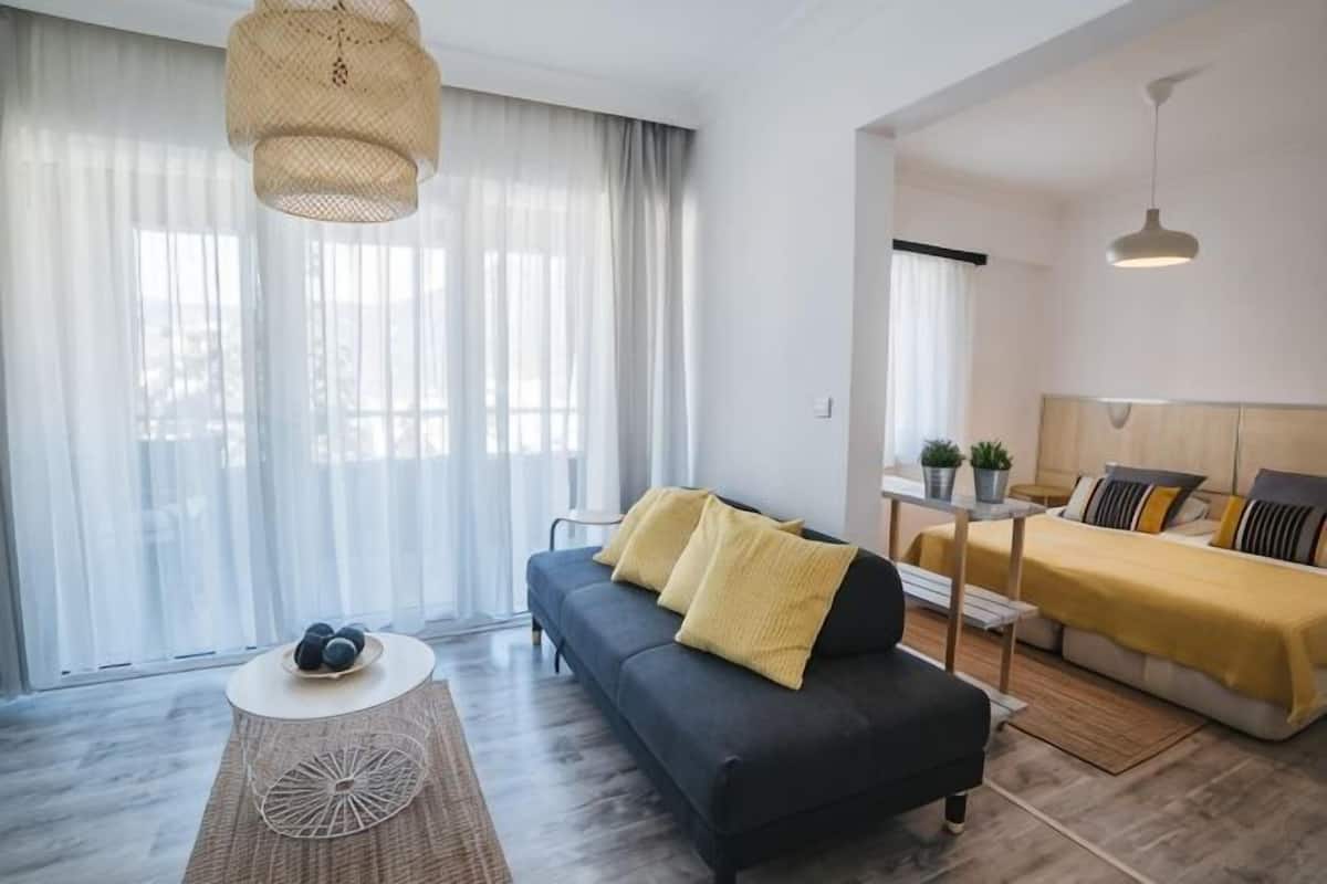 A modern living room with a sofa, a coffee table, and a bed with a yellow blanket.