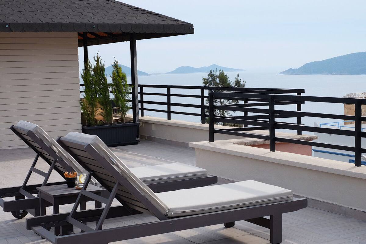 Una terraza en la azotea con dos sillones, una mesita y vistas al mar y a las montañas.