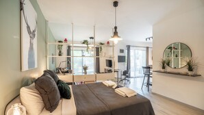 Quarto de hotel moderno com cama, mesa de cabeceira, luminária e vista para a área de refeições.