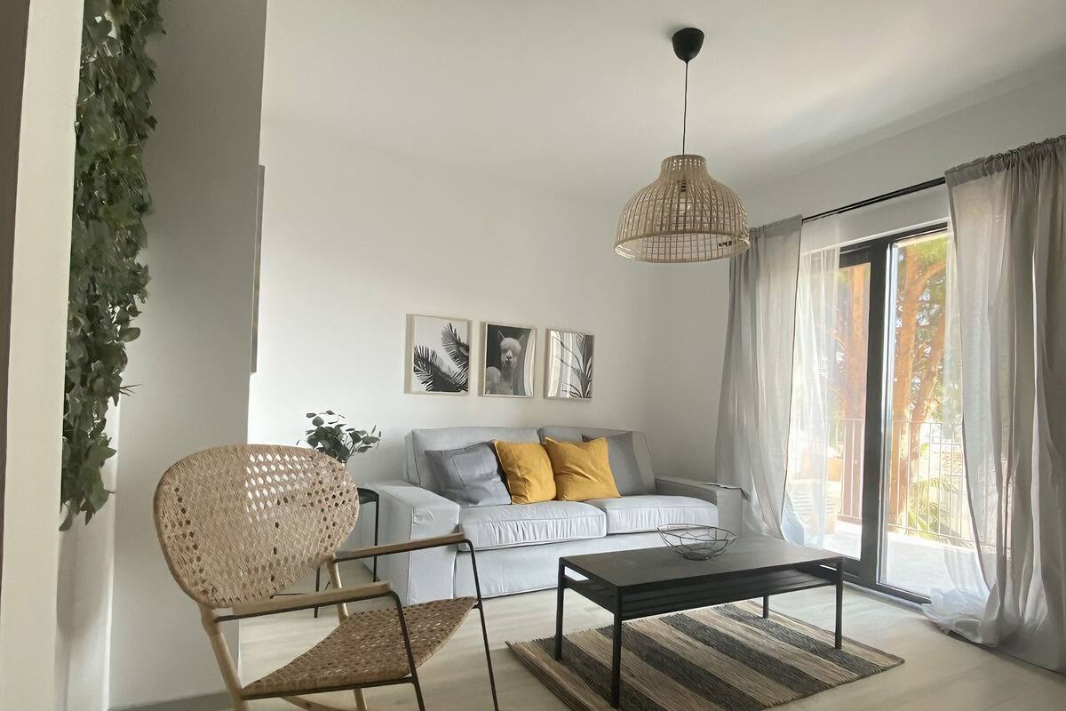 Una sala de estar moderna con un sofá blanco, un sillón mecededor, una mesa de centro y una lámpara colgante.
