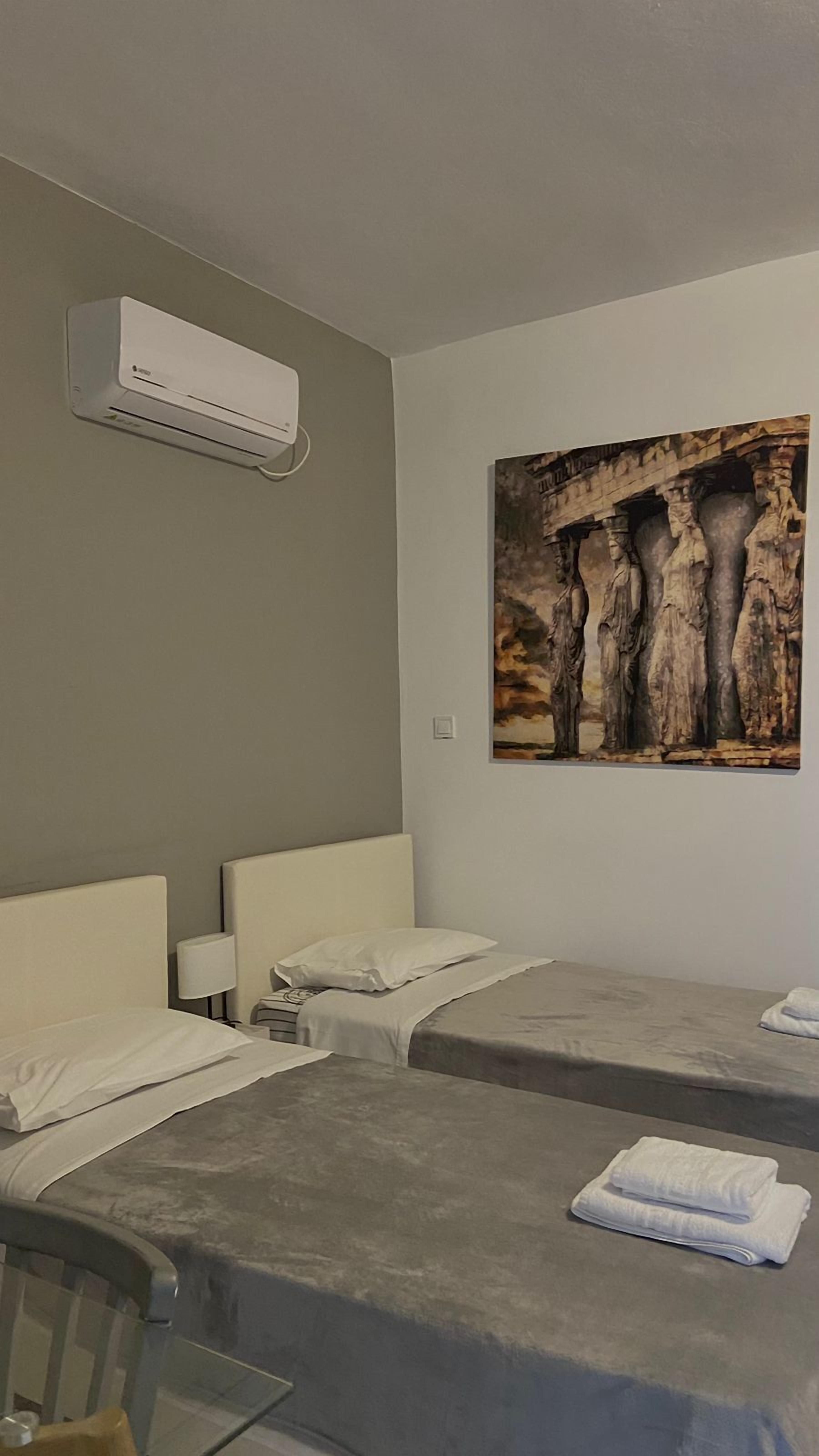 A hotel room with two beds, a wall-mounted air conditioner, and a painting of a tree trunk.