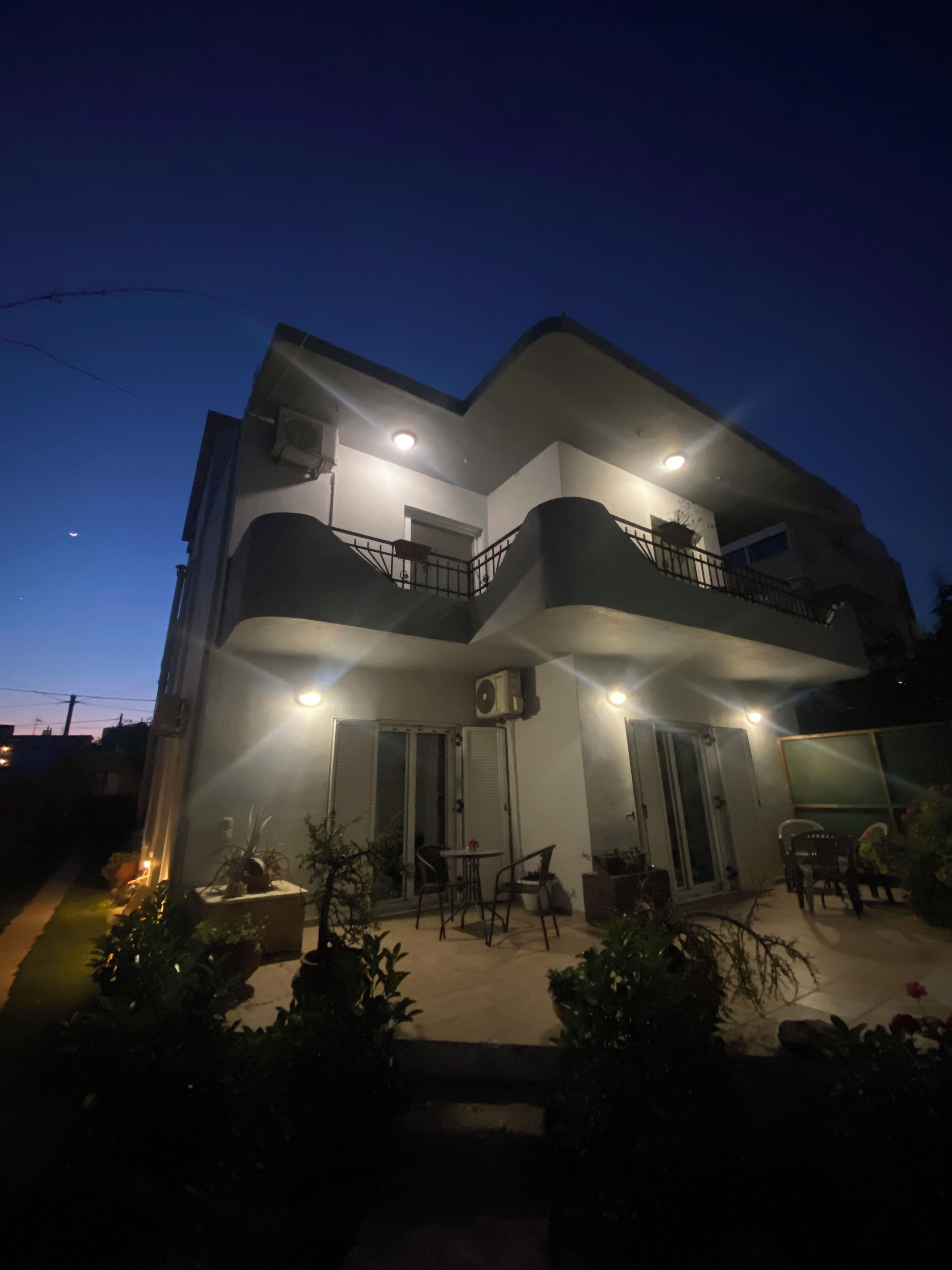 A two-story building with a balcony, outdoor seating, and potted plants.