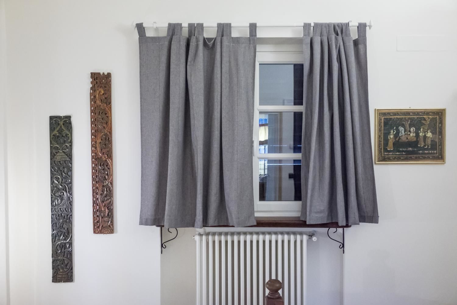A room with a window, grey curtains, a radiator, and two wall decorations.