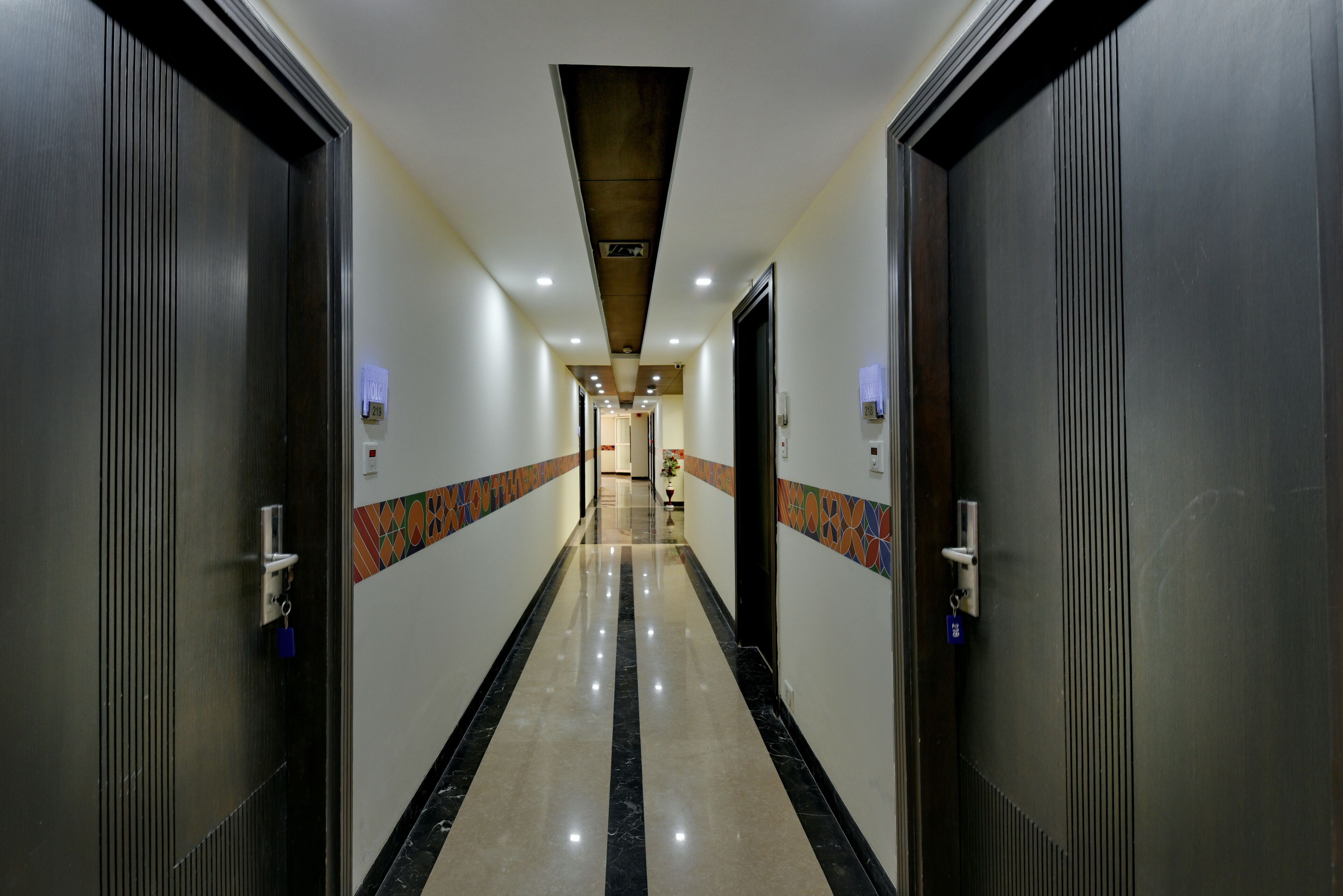 A corridor with doors on both sides, a tiled floor, and a ceiling with recessed lighting.