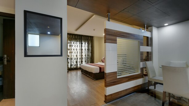 A modern hotel room with a wooden accent wall, a large bed, a sitting area with a chair, and a view of the room's interior. - Hotel Imperial Villa (New Delhi)