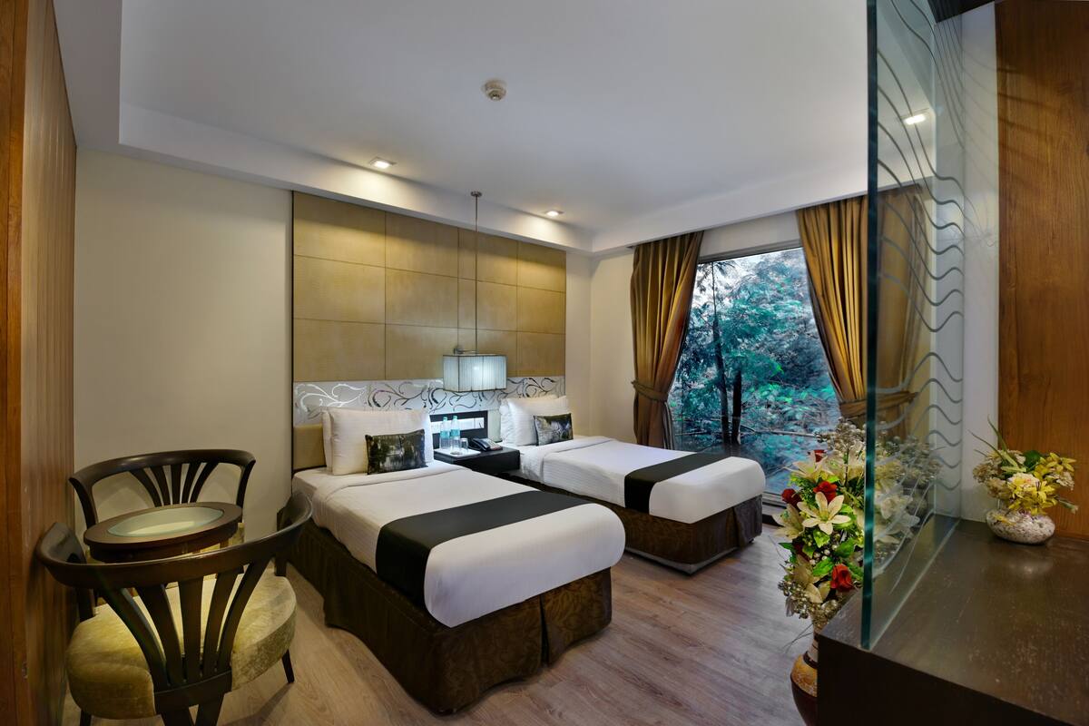 Habitación de hotel con dos camas, una mesita pequeña, una silla y vistas al exterior.