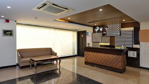 A reception area with a cushioned bench, a reception desk, and a large window. - Hotel Imperial Villa (New Delhi)