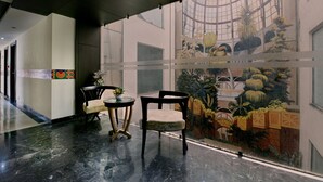 A lobby with a glass wall featuring a botanical mural, a marble floor, and two wooden chairs with a small table. - Hotel Imperial Villa (New Delhi)