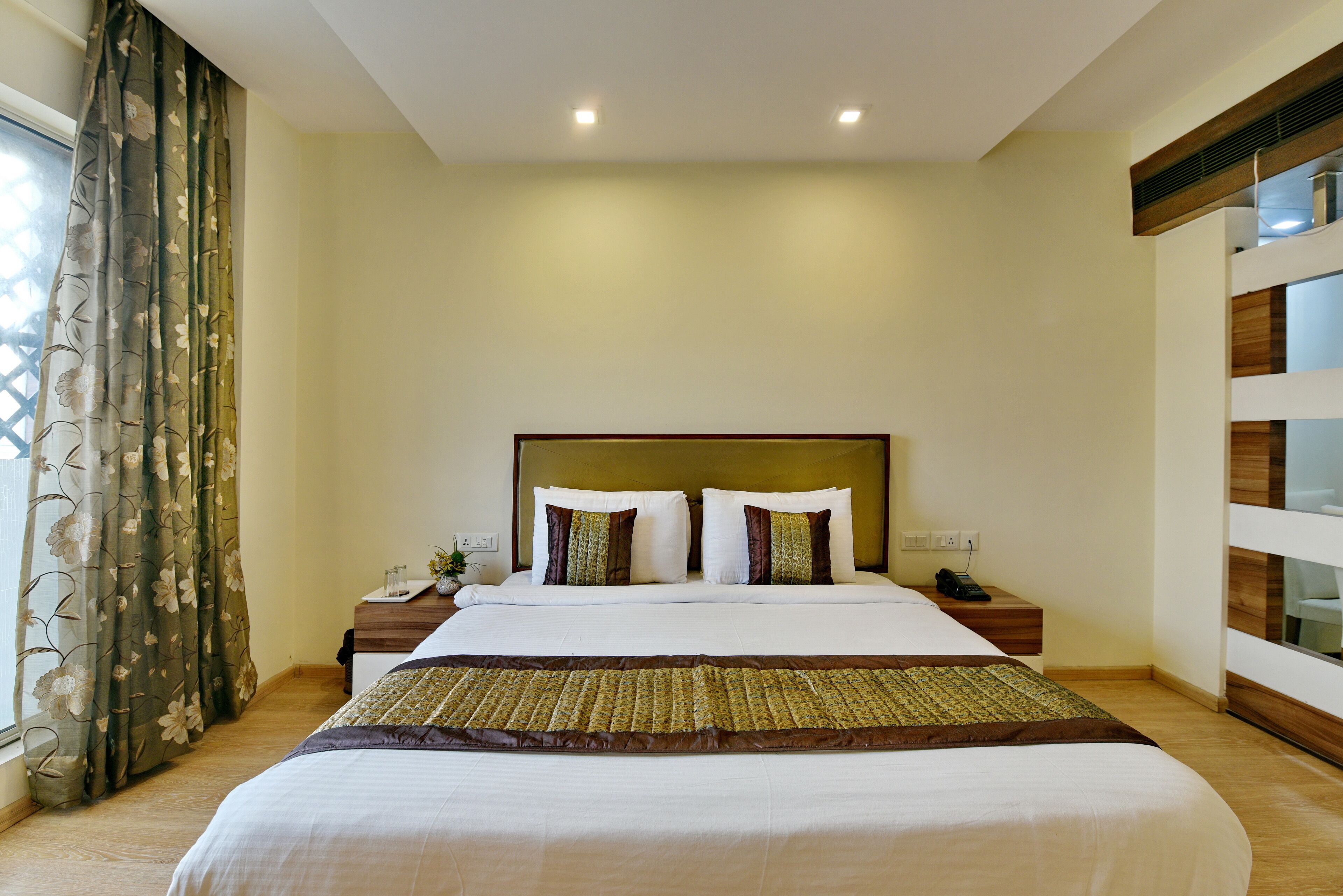 A hotel room with a large bed, a wooden headboard, a nightstand with a phone, and a window with curtains.