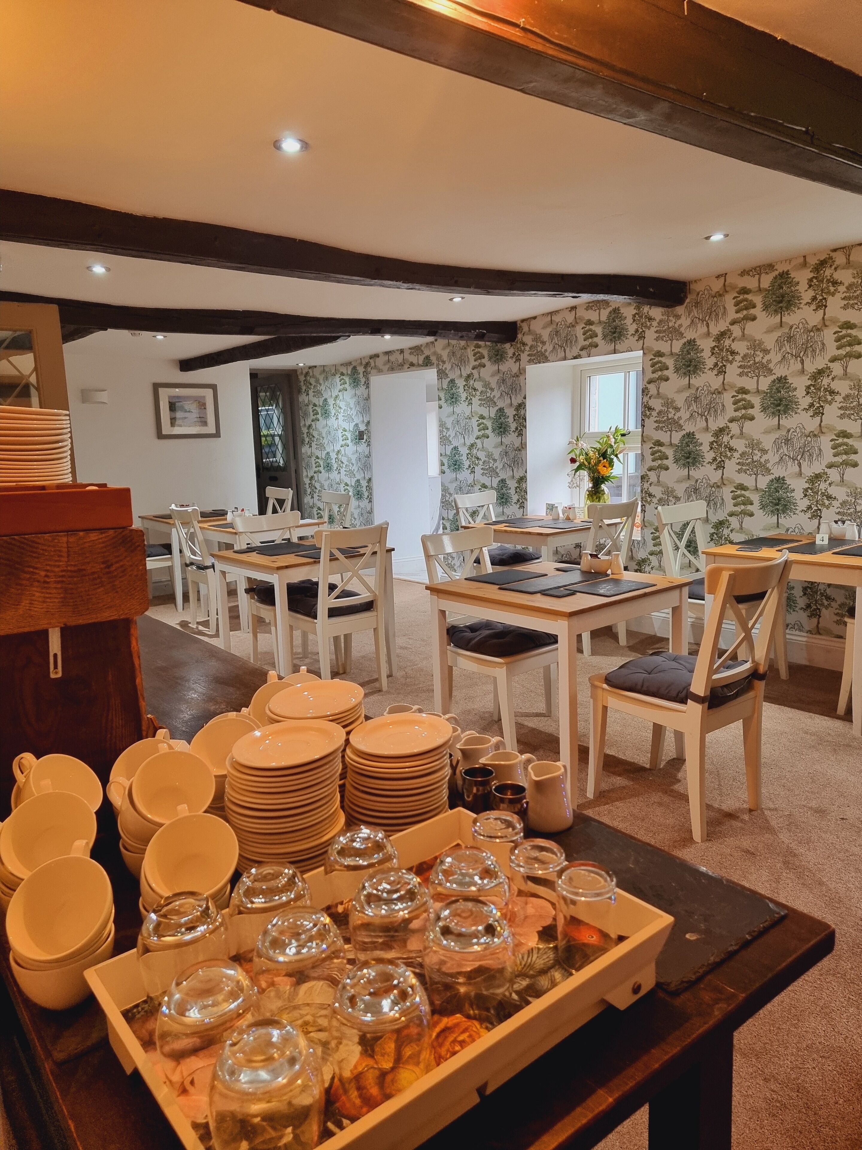 A dining area with tables and chairs, a buffet table with plates and glassware, and a patterned wallpaper.