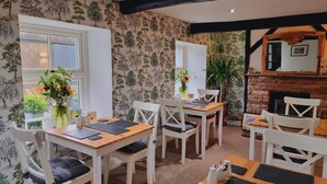 A dining area with white furniture, a brick fireplace, and a wall with a tree pattern. - Lane Head Farm Country Guest House (Penrith)