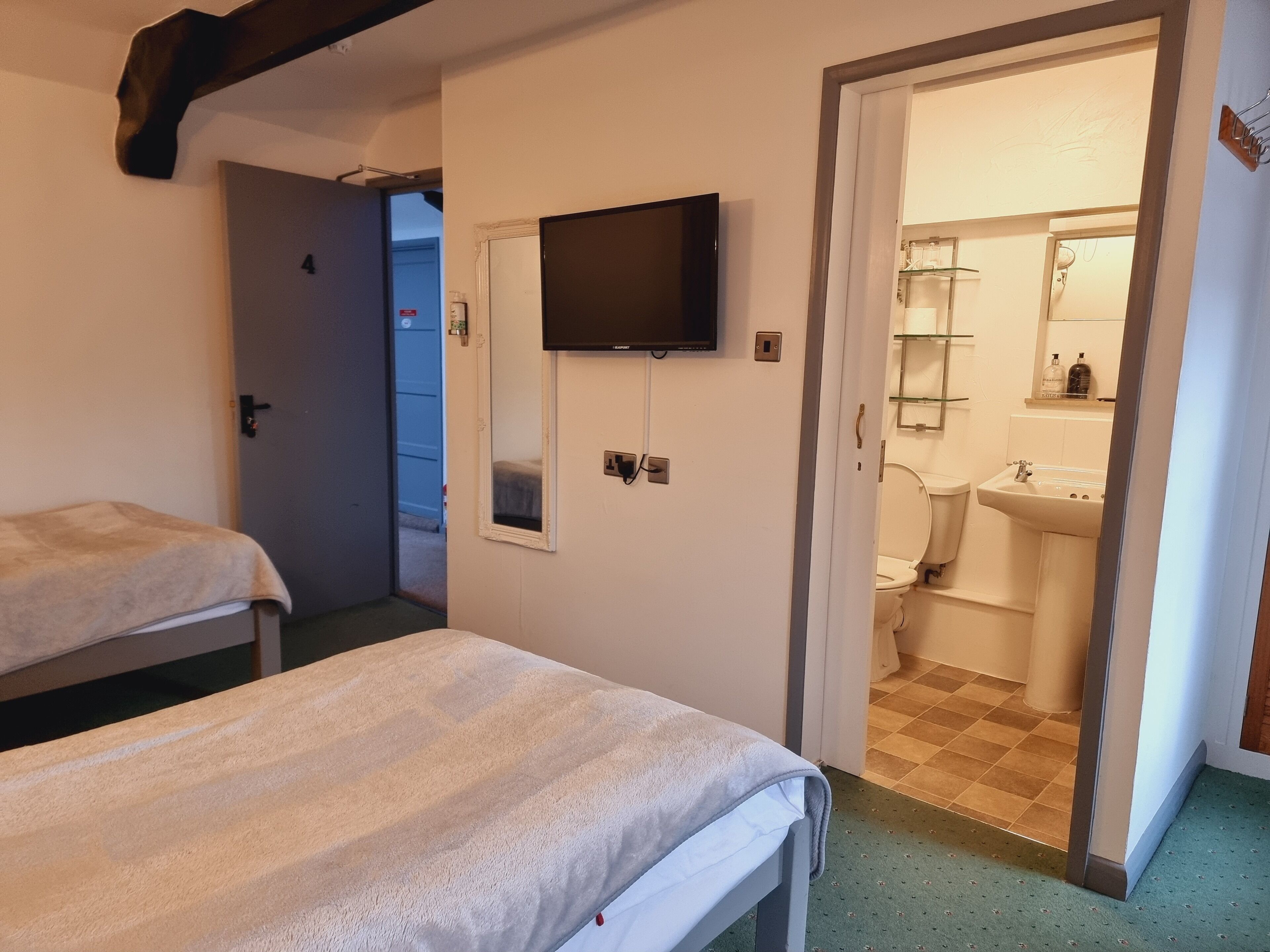 A room with two beds, a television, a bathroom visible through an open door, and a small window.