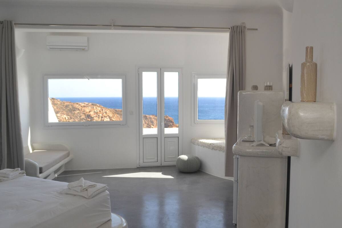 Une chambre d’hôtel dotée d’une grande fenêtre donnant sur la mer et un paysage rocheux.