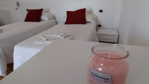 Een hotelkamer met twee bedden, wit beddengoed, rode kussens, een nachtkastje met een roze kaars.