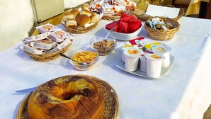 Een tafel buiten gedekt met diverse etenswaren, zoals brood, gebak en een taart, op een witte tafeldoek.