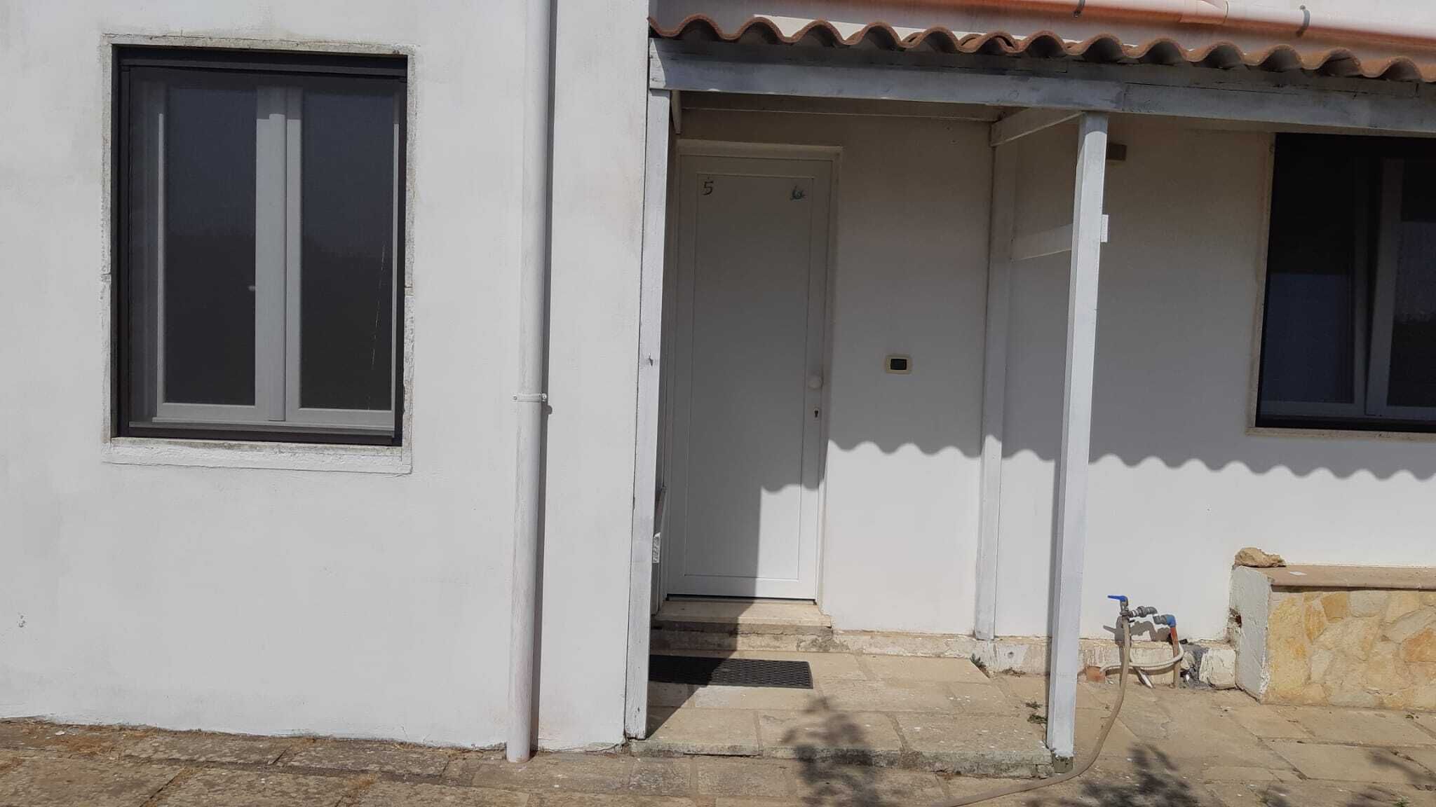 A white building with a single window and a door leading to a covered entrance.
