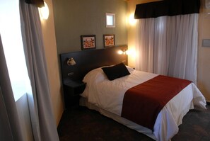A hotel room with a bed, a nightstand, a wall-mounted lamp, and two framed pictures. - Complejo Barraquero (Mendoza)