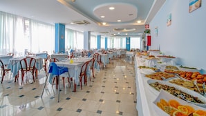 A spacious dining area with multiple tables and chairs, a buffet line with various food items, and a bright, well-lit interior with large windows. - Hotel Ervill (Rimini)