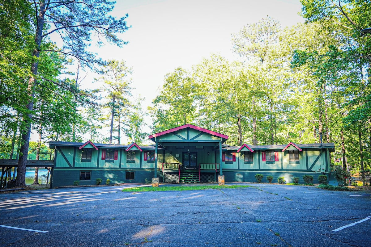 A two-story lodge with a green exterior and red trim, featuring a porch and a small front yard.